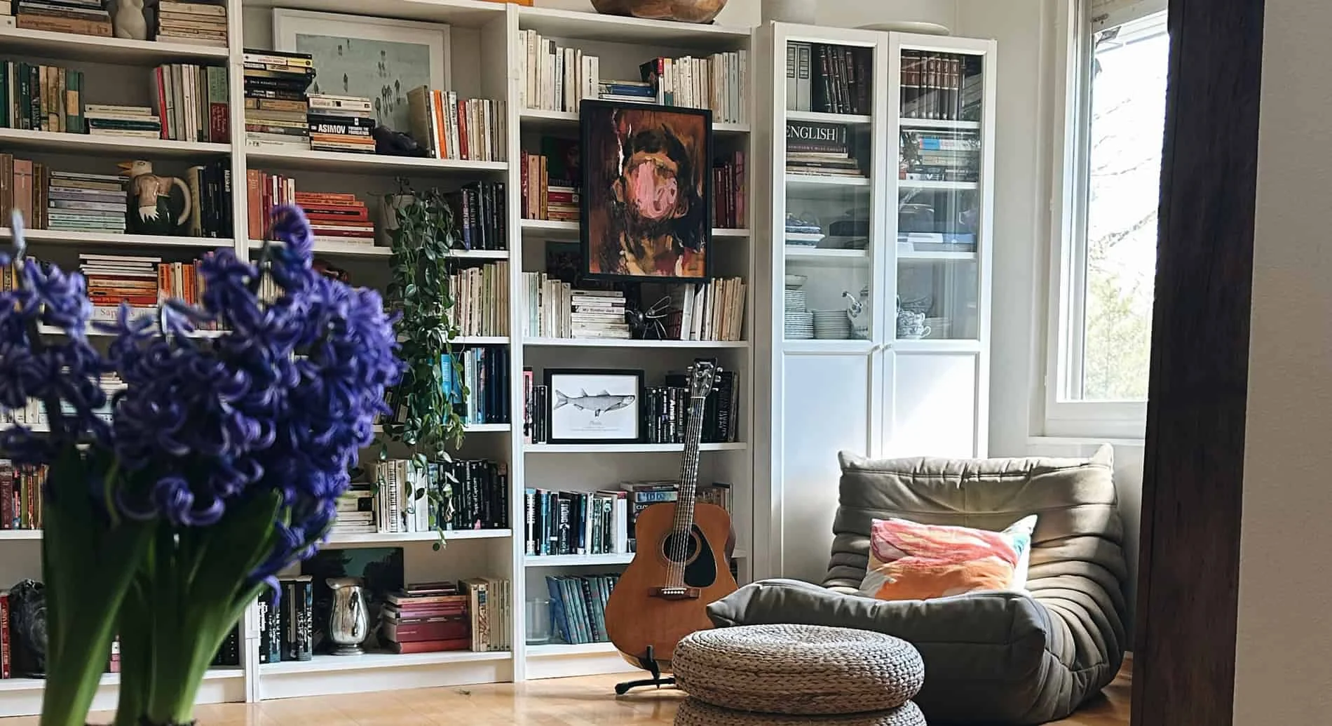 A cozy living room featuring a large bookshelf filled with books, a guitar, and a comfortable armcha.
